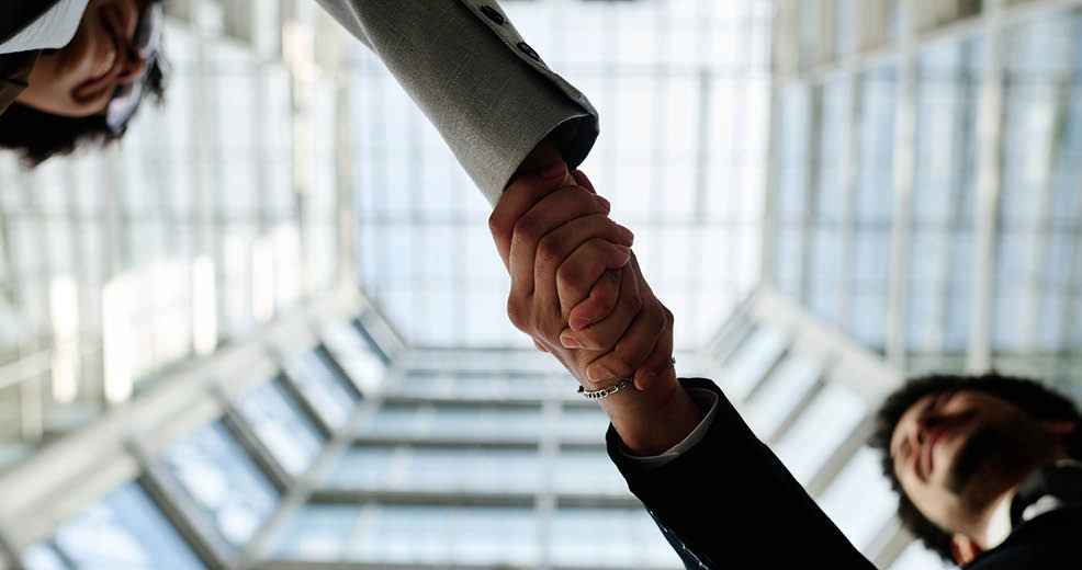 Low angle view of young business people shaking hands to each other standing in modern office building